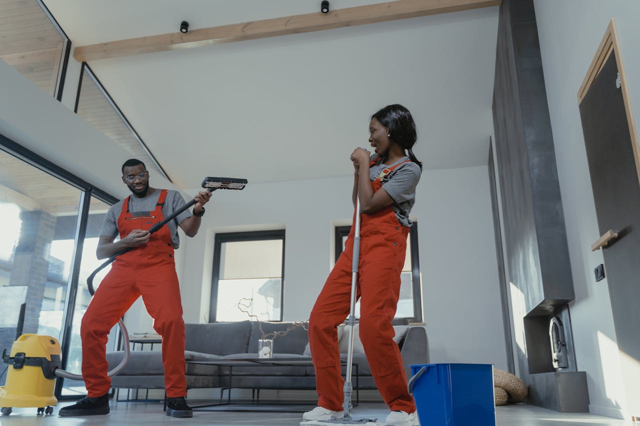 hero-img Two adults in vibrant coveralls cleaning a modern home interior, enjoying work.