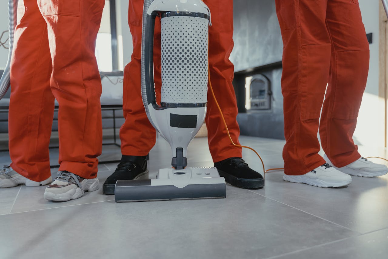 services-01 Team of professional cleaners in red uniforms using a vacuum cleaner indoors.